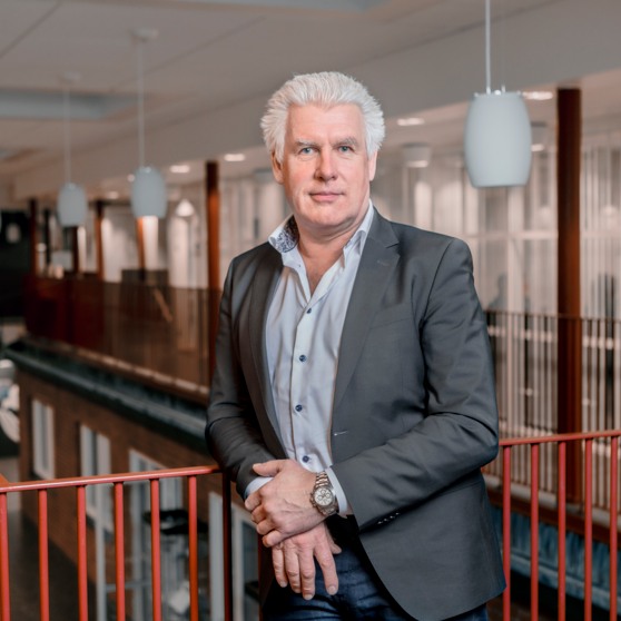 Kommundirektör Anders Björlin i kommunhuset. Han har grå kavaj och står framför ett rött räcke. 